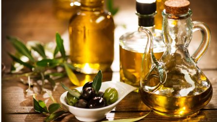 Bottiglie di olio extravergine d’oliva e olive fresche su tavolo in legno, illuminate da luce calda.